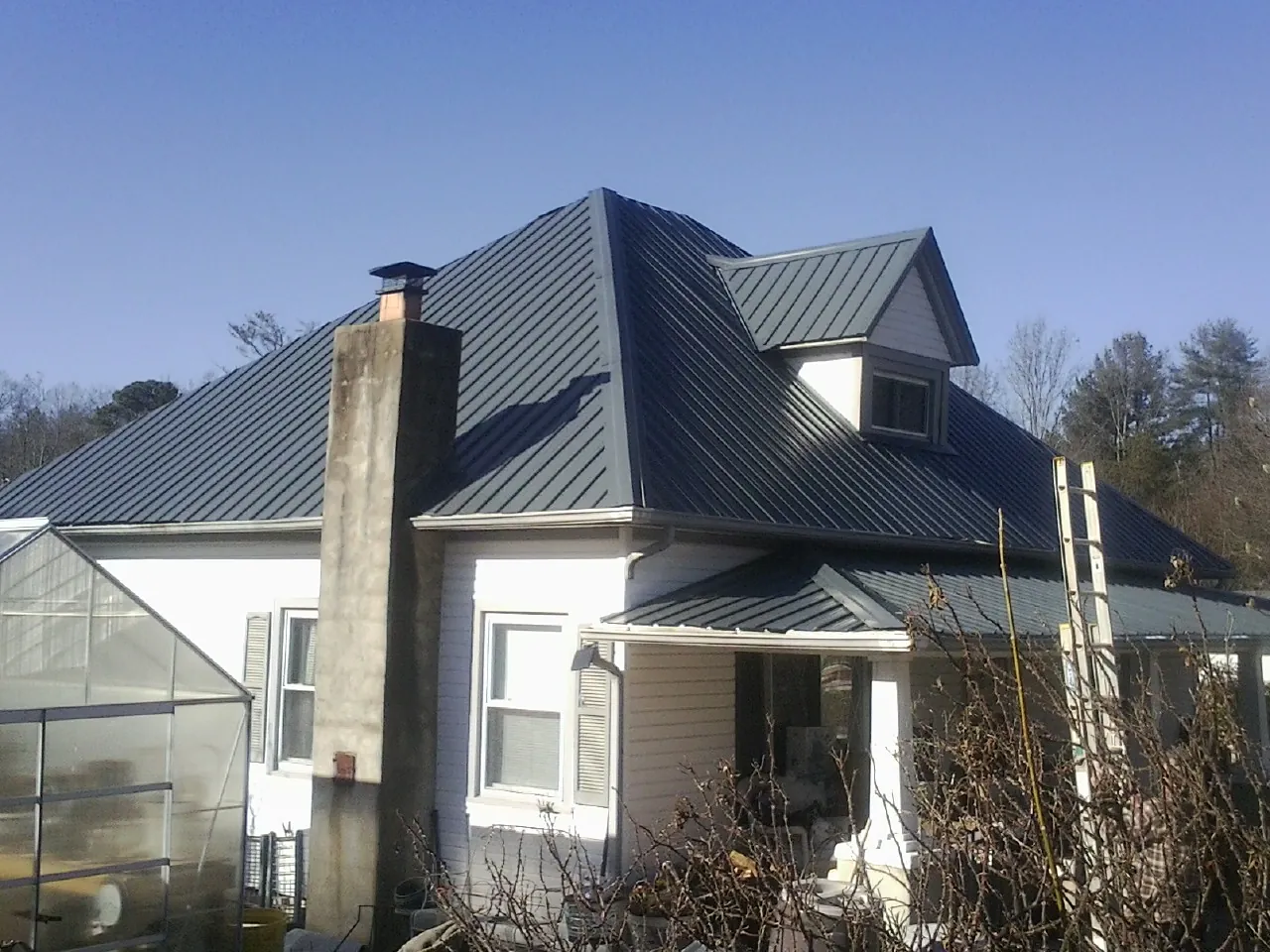Dark blue standing seam metal roof on a white farmhouse with dormer — Slate & Tile Roof Repair by Roofing Brothers in Double Springs