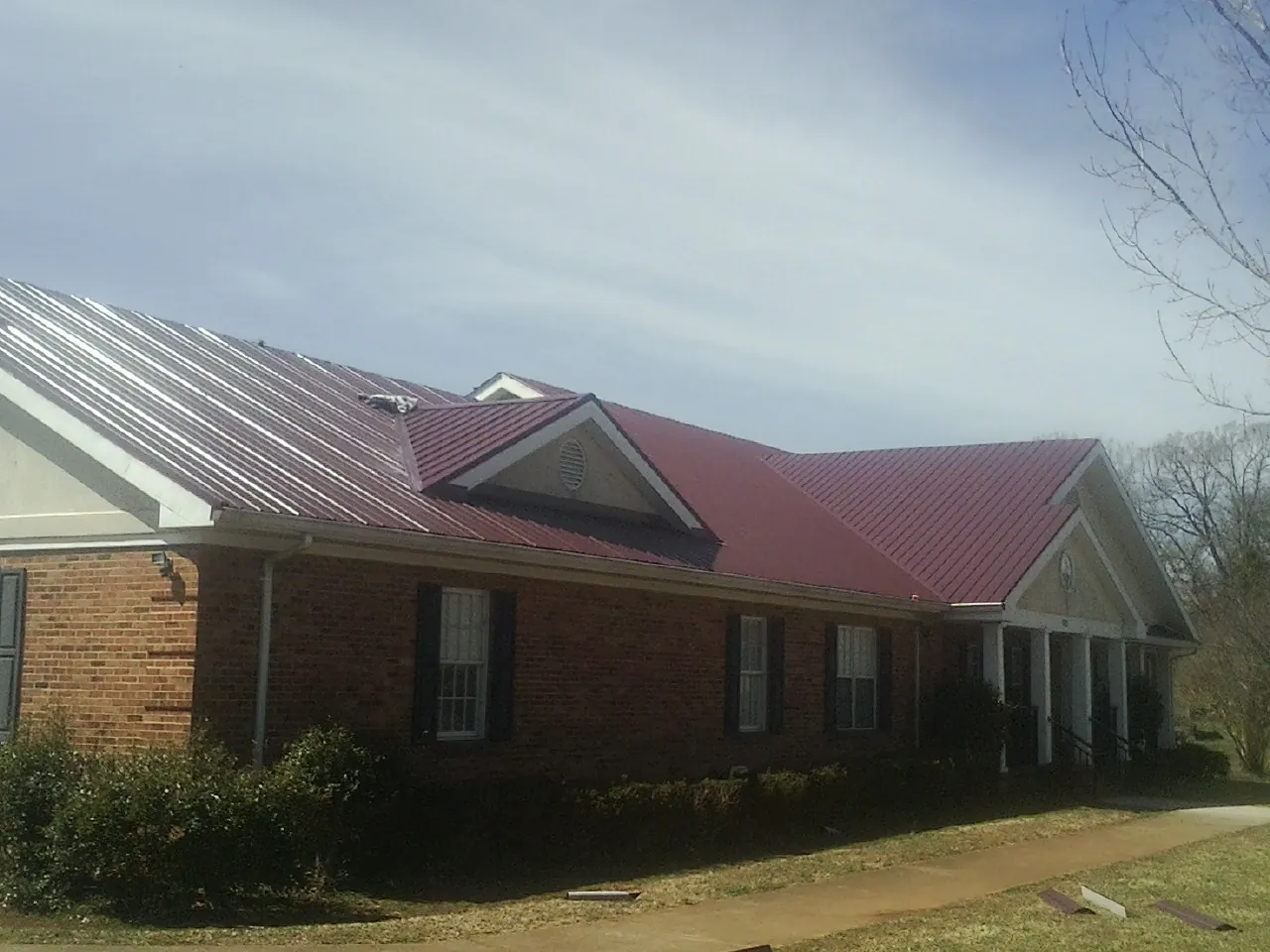 Red metal roof with gabled entries on a long brick building, from a Hail Damage Roof Repair job in Double Springs