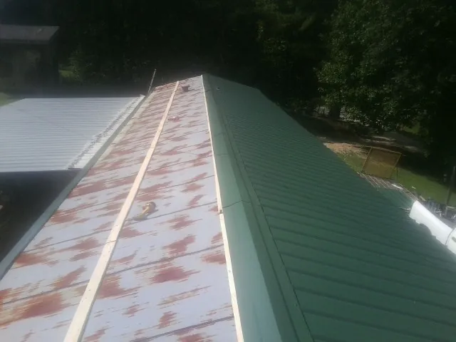 Old rusted panels beside newly installed green metal roofing — Wind Damage Roof Repair by Roofing Brothers in Double Springs