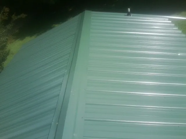 New green metal panels meeting at the ridge of a roof — Flat Roof Repair work by our crew in Double Springs