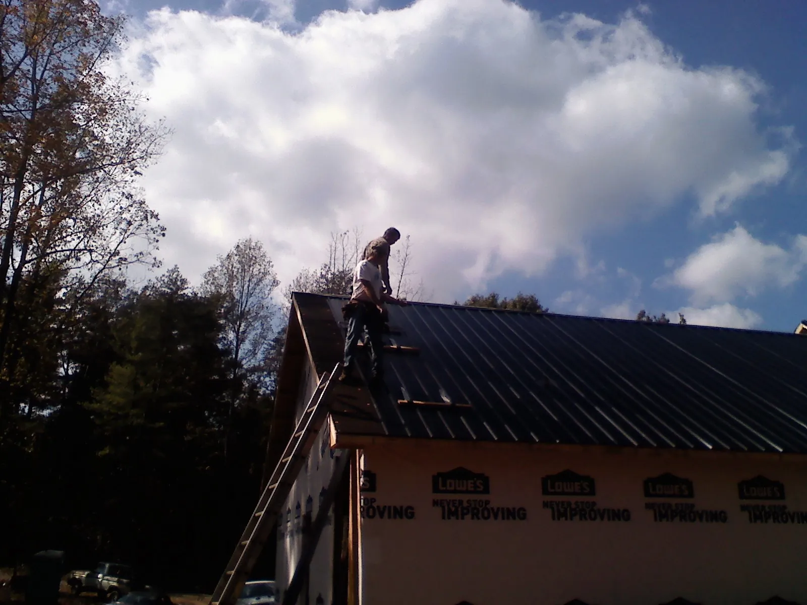 Roofer fastening dark metal panels high against a cloudy sky, from a Roof Inspection job in Double Springs