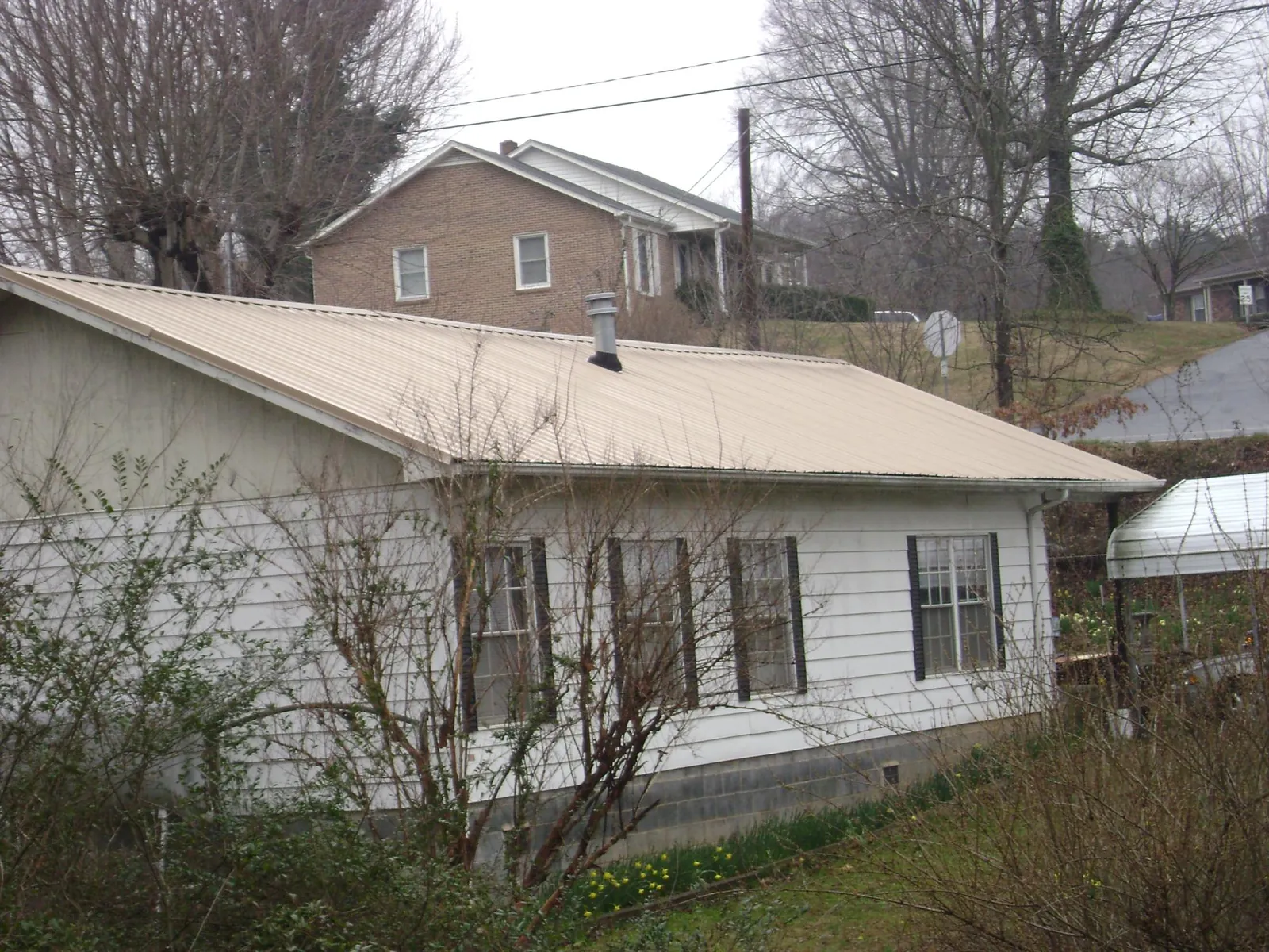 Tan metal roof on a white sided house set into a hillside — Commercial Roofing by Roofing Brothers in Double Springs