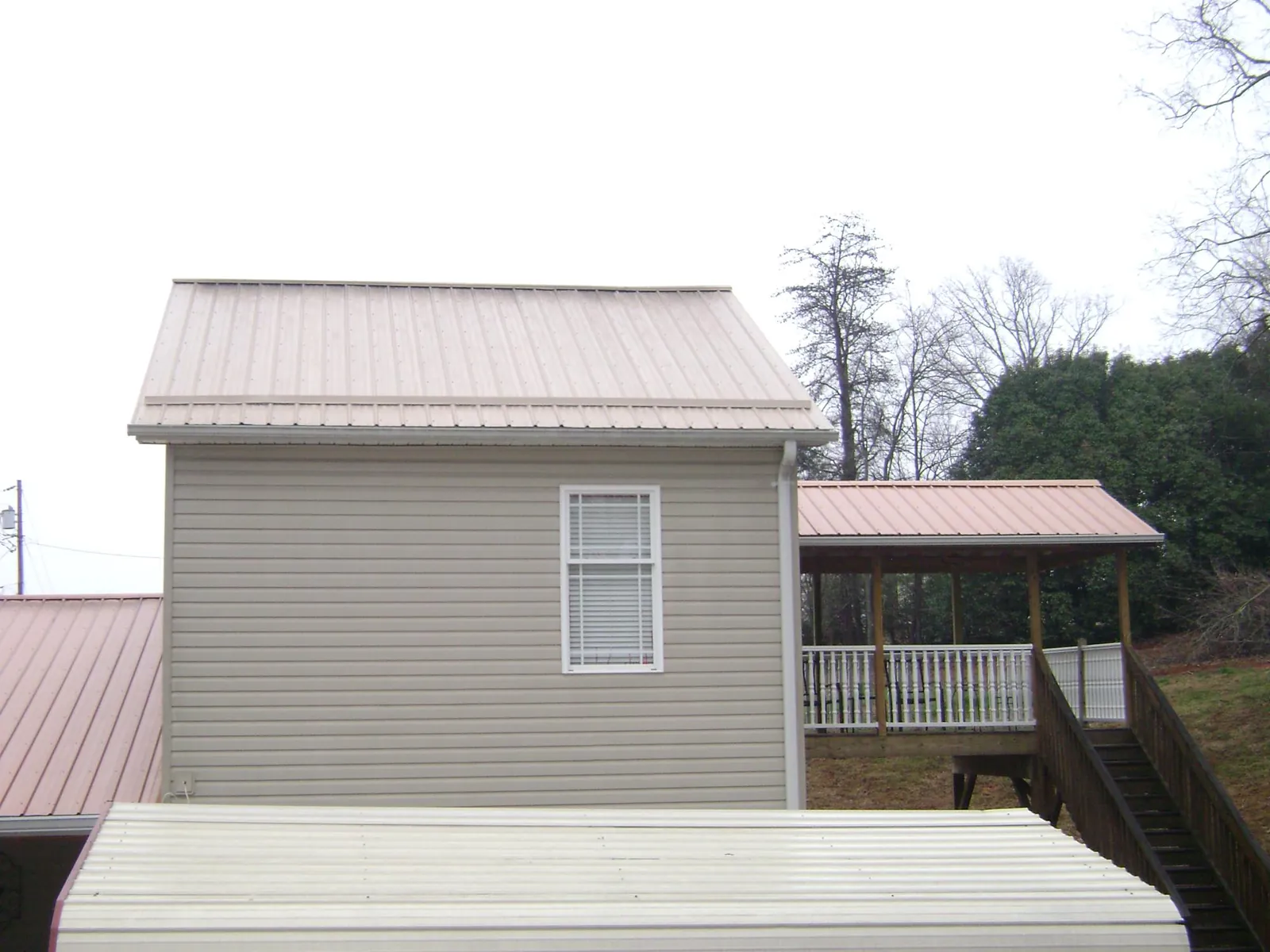 Tan metal roofs on a two story addition and attached porch, from a Roof Replacement job in Double Springs
